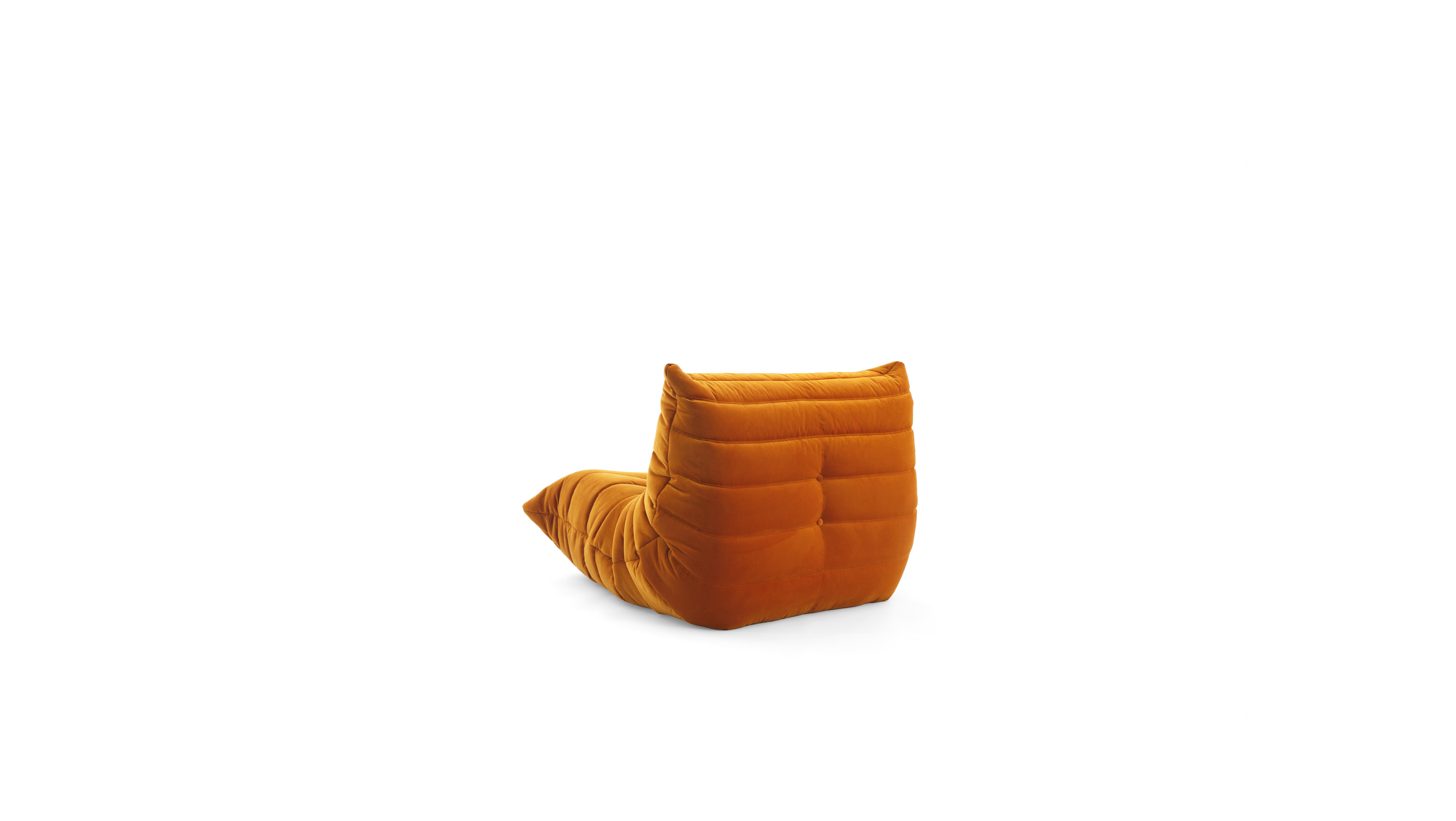 An orange velvet TOGO fireside modular lounge chair with a low, thick backrest and a tapered seat, shown from a side angle on a plain white background.